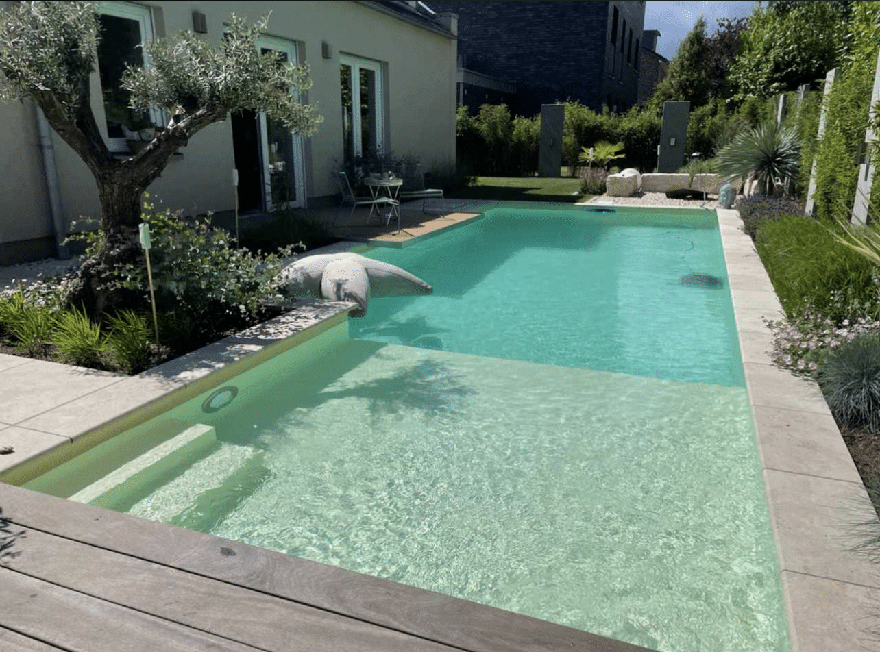 Ein rechteckiger Pool im Hinterhof mit klarem Wasser und Folienauskleidung, einer Treppe, die hineinführt, und einem Terrassenbereich, der von Grün und moderner Landschaftsgestaltung umgeben ist. Es gibt einen kleinen Tisch und Stühle in der Nähe des Hauses.