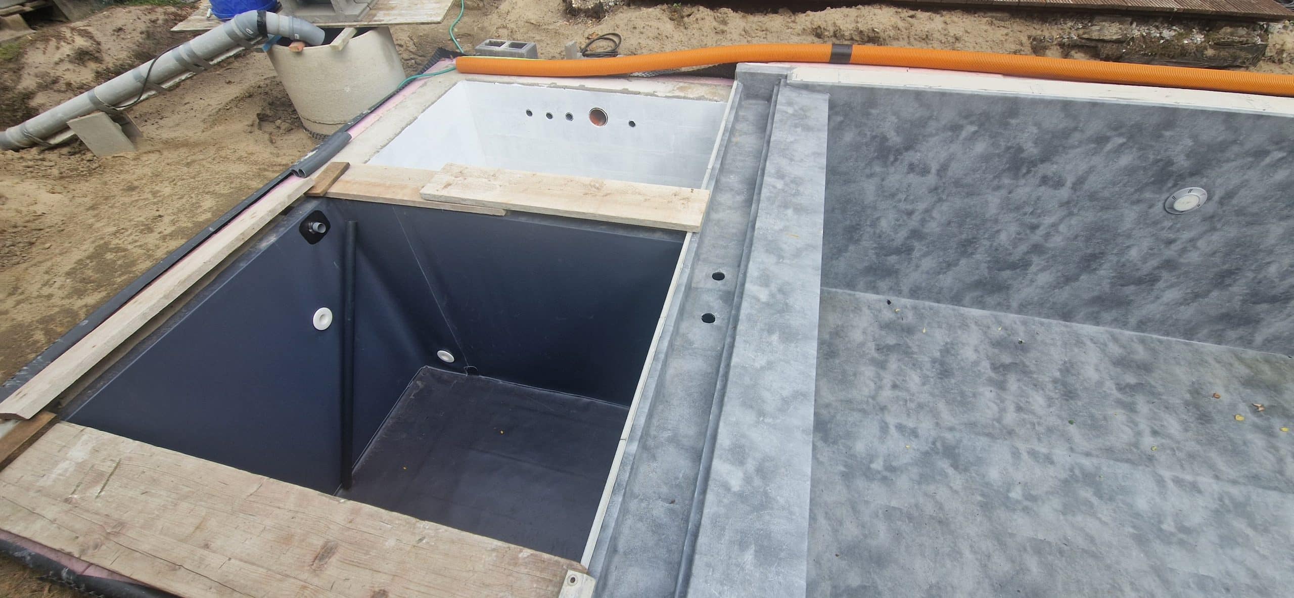 Ein teilweise gebauter Pool mit freiliegenden Rohrleitungen, Holzbrettern auf der Oberseite und unfertigen Oberflächen. Um den Pool herum sind Sand und Baumaterialien zu sehen, die die laufende Installation von teich folie verdeutlichen.